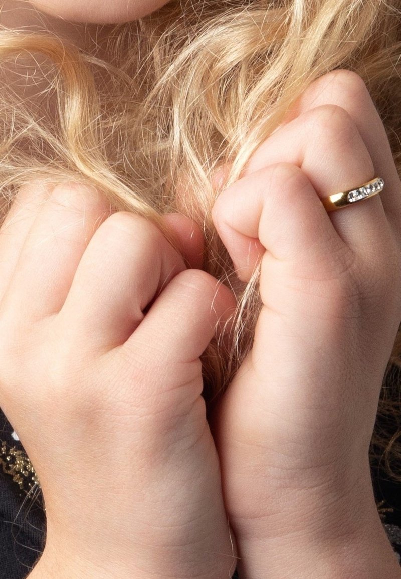 Gouden ring met een glanzend oppervlak en ingelegde stenen, gedragen aan een hand die lange, golvende, blonde haren vasthoudt, met een mooie huidstructuur.