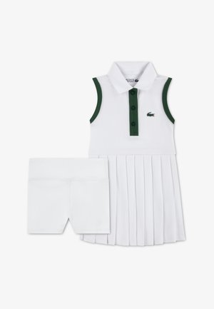 Robe polo blanche avec accents verts, jupe plissée et fermeture à trois boutons. Comprend un short blanc assorti pour plus de couvrance.