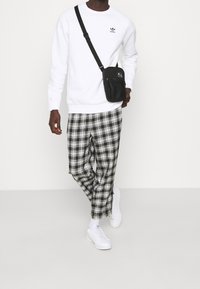 Vit sweatshirt med en liten svart logotyp, svartvita rutig byxor, vita sneakers och en svart axelväska.