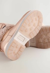 Botas de invierno de color rosa claro con un borde esponjoso, suelas gruesas con un diseño de tacos en forma de estrella y la marca "Baker" en la suela.