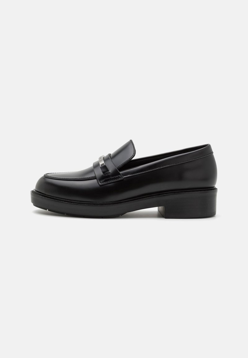 Mocassins en cuir noir avec un bout rond, un accent argenté sur la bride, et un petit talon bloc. Texture lisse avec des détails de couture minimalistes.