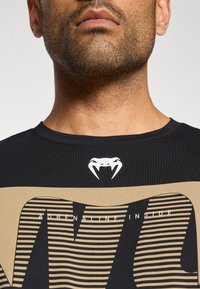 Zwart T-shirt met een ronde hals, met een slanglogo in wit en horizontale strepen in beige, met de tekst "ADRENALINE INSIDE".