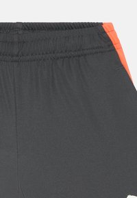 Pantaloni sportivi neri con cintura elastica, caratterizzati da un accento laterale arancione e un tessuto leggero e morbido, adatto per l'abbigliamento attivo.