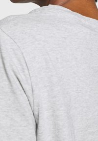 T-shirt di cotone grigio con una texture liscia, caratterizzato da un collo rotondo e una vestibilità comoda. Il tessuto mostra un delicato motivo mélange.