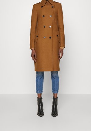 Brązowy, dwurzędowy płaszcz z czarnymi guzikami, dwoma bocznymi kieszeniami i kołnierzem. Noszony na jasnoniebieskie, ścięte dżinsy i czarne botki za kostkę.