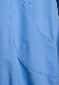 Nærbillede af lyseblåt stof med synlige syddede sømme, der danner buede og lige linjer.