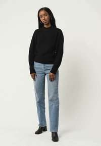 Schwarz gestreifter Pullover mit Rundhalsausschnitt, kombiniert mit hellblauen geraden Jeans und schwarzen, ankle boots mit Absatz.