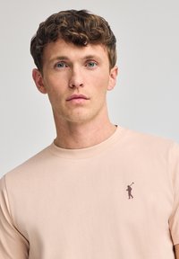 Lichtroze langemouw shirt van zacht materiaal met een ronde hals en een klein logo in een donkerder roze dat op de borst is gedrukt.