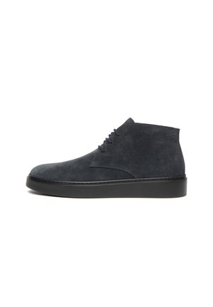 Bottine en daim gris anthracite foncé, à lacets noirs et à épaisse semelle noire, présentée de profil sur un fond blanc.