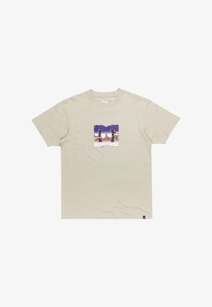 Beige Baumwoll-T-Shirt mit kurzen Ärmeln und einer quadratischen Grafik, die die Buchstaben DC in Lila und Weiß vor einem abgestuften Hintergrund zeigt.