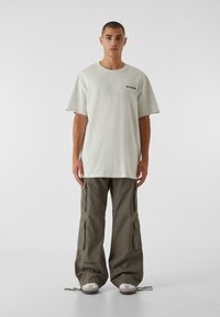 Lys grå oversized t-shirt med korte ærmer, parret med løse, olivengrønne cargo bukser med flere lommer og justerbare manchetter.
