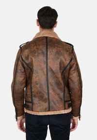 Giacca in finta pelle marrone con colletto in shearling. Presenta accenti neri, una finitura testurizzata e dettagli con cerniere. Vista posteriore mostrata.