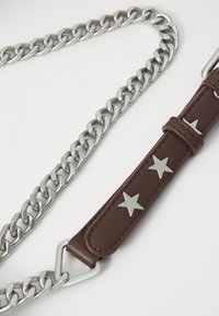 Cinturino in pelle marrone con dettagli a stella argentati collegato a una catena argentata. Il cinturino è testurizzato e presenta un anello metallico triangolare.