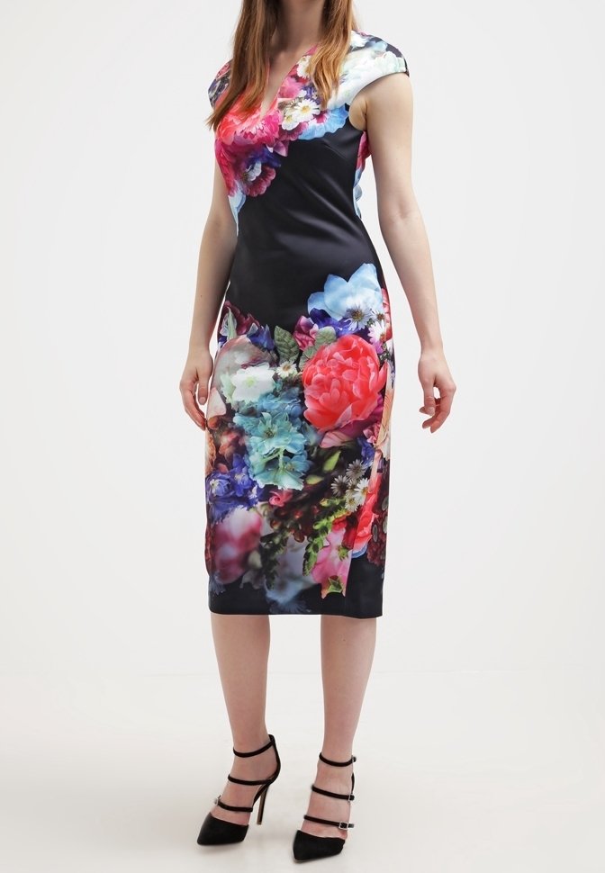 Blumendruckkleid mit taillierter Silhouette, kurzen Ärmeln und einer Mischung aus lebendigen Farben auf dunklem Hintergrund, kombiniert mit schwarzen Absätzen.