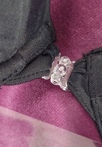 Tessuto nero con una finitura texturizzata presenta una fibbia in plastica trasparente. Lo sfondo è un morbido materiale viola.