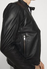 Svart läderjacka med en figursydd design, hög krage och fickor med dragkedja. Har en mjuk yta och synliga sömdetaljer.