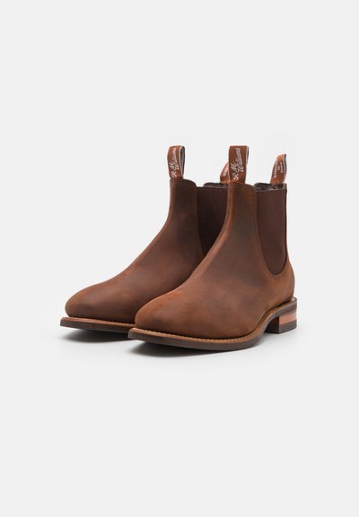 Botas Chelsea de cuero marrón con paneles laterales elásticos, punta redondeada y tiradores. Presentan un tacón bajo apilado y un acabado suave.
