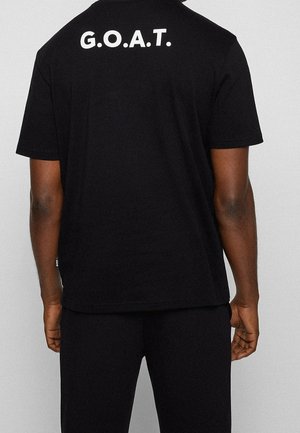T-shirt en coton noir avec les lettres blanches "G.O.A.T." au dos. Manches courtes et coupe décontractée, avec une texture lisse.