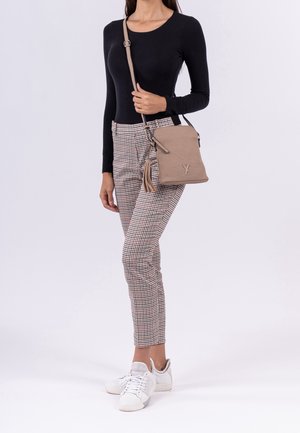 Mujer con camiseta de manga larga negra, pantalones ajustados a cuadros, zapatillas blancas y bolso cruzado beige con detalle de borlas.