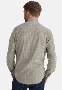 Grün-braun kariertes Hemd mit langen Ärmeln, geknöpften Manschetten und abgerundetem Saum. Verfügt über einen Schulterbereich und einen strukturierten Stoff.