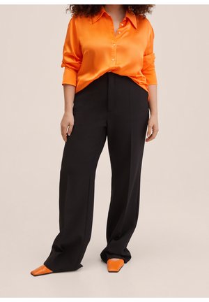 Chemise satinée orange vif avec des détails de boutons, associée à un pantalon large noir et des chaussures pointues orange. Texture lisse, coupe décontractée.