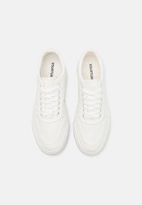 White canvas sneakers with round toes, flat laces, and subtle stitching details. The interior features a contrasting brand label.