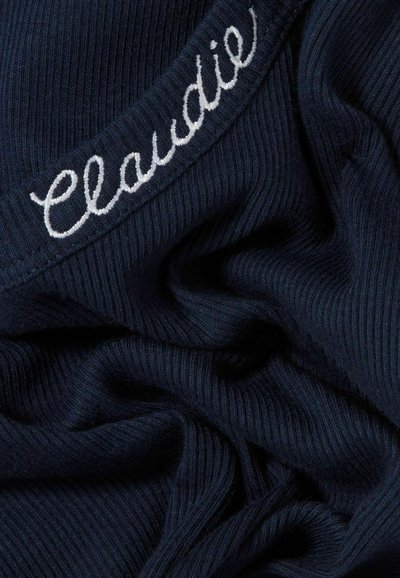 Tejido de canalé azul marino con detalle bordado en blanco que dice "Claudie", con una superficie suave y texturizada y pliegues suaves.