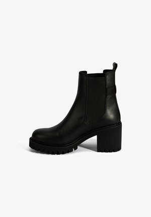Bottine en cuir noir avec des panneaux latéraux élastiques, un talon bloc épais et une semelle en caoutchouc texturé pour une meilleure traction. Design minimaliste.