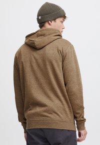 Bruine hoodie van textuurstof met een capuchon, met een relaxed fit en geribbelde manchetten. Draag met een olijfgroene gebreide beanie.