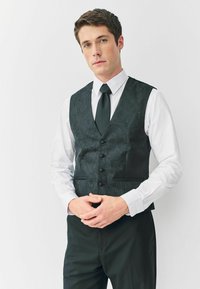 Fekete mintás mellény paisley mintával, öt gombbal, fehér ing fölött viselve, fekete nyakkendővel és nadrággal kiegészítve.