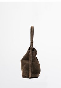 Borsa a secchiello in suede marrone con tracolla regolabile, in piedi su uno sfondo bianco semplice.