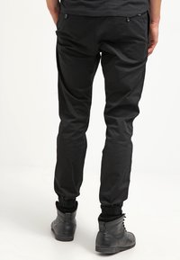 Svarta byxor med smal passform, elastiska mudd, och två bakfickor, parat med svarta läderstövlar med en texturerad yta.