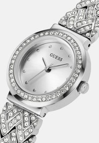 Sølvur med rund skive, krystalaccenter omkring bezelen og et tekstureret armbånd med hævede diamantmønstre.