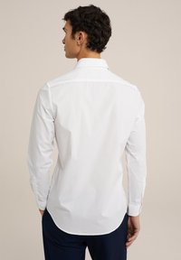 Witte overhemdd met lange mouwen, ronde zoom en knopen bij de manchetten, gemaakt van zachte stof, met een klassiek kraagontwerp.