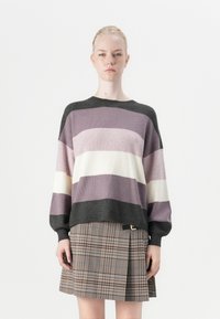 Knitted sweater in purple, cream, and dark gray stripes; oversized fit with ribbed texture. Paired with a plaid skirt featuring a side buckle.