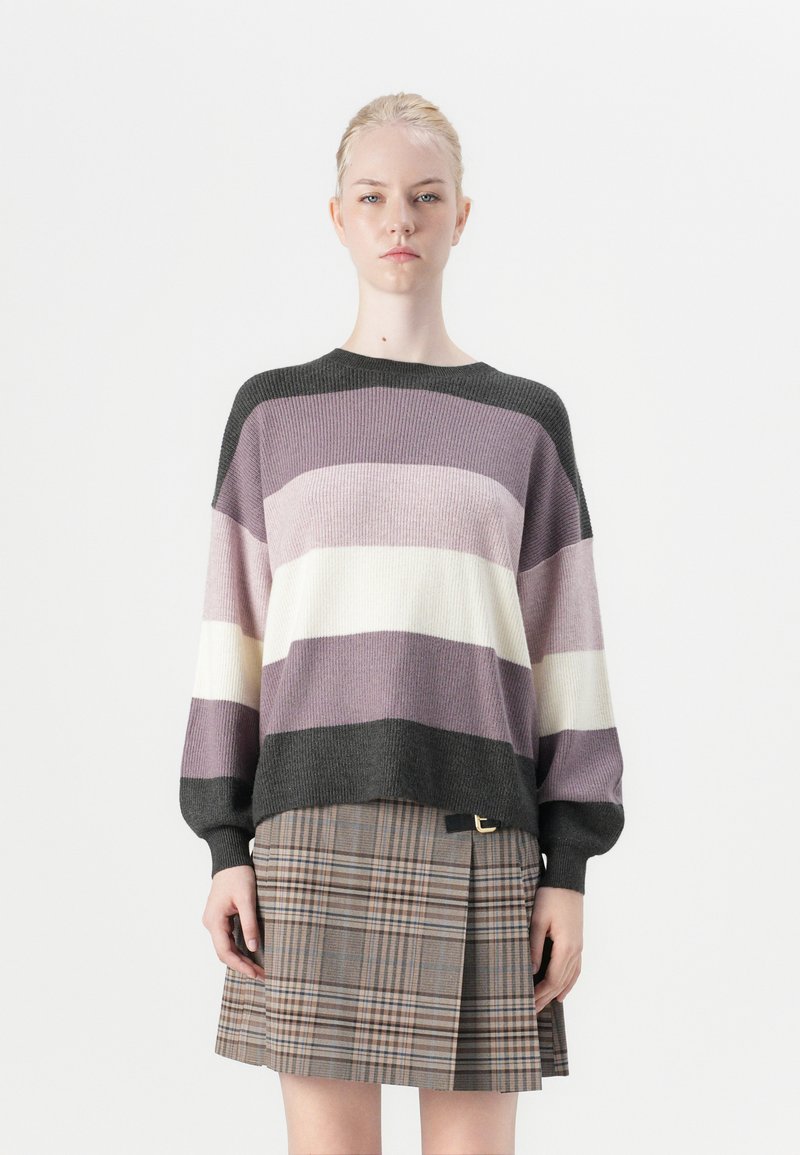 Knitted sweater in purple, cream, and dark gray stripes; oversized fit with ribbed texture. Paired with a plaid skirt featuring a side buckle.