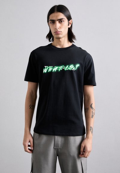 Schwarzes Baumwoll-T-Shirt mit einem neon-grünen grafischen Text "WAS IST LOS?" über der Brust. Klassischer Rundhalsausschnitt, kurze Ärmel, lässige Passform.