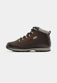 Bota de senderismo de cuero marrón con ojales de metal, acentos grises, suela de goma y un tirador trasero. Presenta materiales texturizados y un diseño resistente.