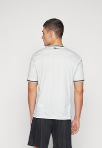 Lichtgrijze sportshirt met korte mouwen, een ronde halslijn en subtiele grafische textuur; gecombineerd met zwarte shorts.