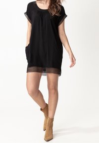 Vestido negro con mangas cortas, que incluye bolsillos y un borde de encaje texturizado en el dobladillo. Combinado con botas de tobillo marrón claro.