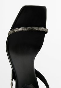 Sandal alto nero con tacco, caratterizzato da una fascia metallica testurizzata e un design a punta quadrata, con una finitura in pelle liscia e una suola robusta.