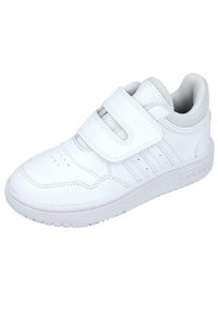 Baskets blanches avec une tige en cuir lisse, des brides Velcro, une pointe perforée et une semelle en caoutchouc texturé arborant un logo discret sur le côté.