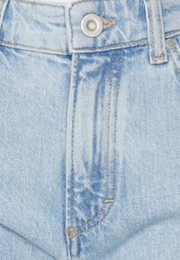 Los jeans de mezclilla azul claro presentan una cintura alta, un botón de metal plateado y costuras en naranja contrastante a lo largo de las costuras y los bolsillos.