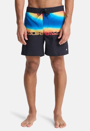 Męskie kąpielówki z gradientowym wzorem od niebieskiego do pomarańczowego, z czarnym, jednolitym dołem i wyraźnym różowym logo. Elastyczny pas z sznurkiem do regulacji.