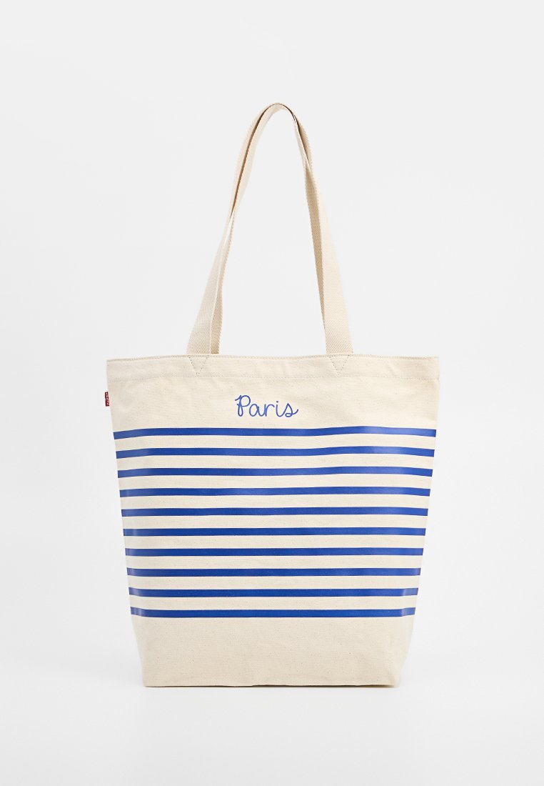 Borsa tote in canvas color crema con strisce orizzontali blu e la scritta "Paris" ricamata in corsivo. Presenta due manici robusti.