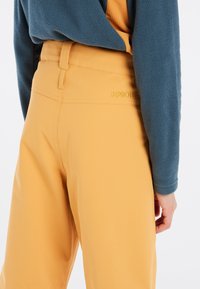 Geel zachte-shell broek met een gladde textuur, voorzien van een middelhoge tailleband en een klein logo op de achterkant.
