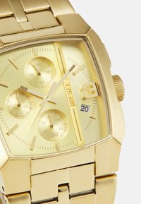 Goldfarbene Metalluhr mit quadratischem Gehäuse, strukturiertem goldenen Zifferblatt, drei Unterzifferblättern und Datumsanzeige. Ausgestattet mit einem passenden goldfarbenen Gliederarmband.