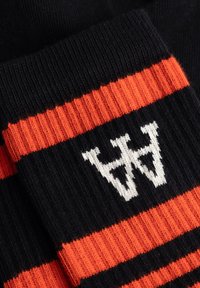 Sort strikket stof med orange vandrette striber og et hvidt stiliseret "W" mønster strikket i midten.