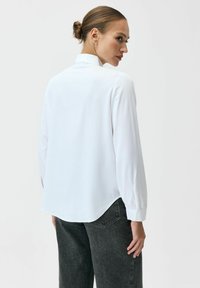 Biała koszula z długim rękawem, prostym dołem, mankietami na guziki oraz wysokim kołnierzem, w zestawie z szarymi spodniami z wysokim stanem. Gładka faktura.