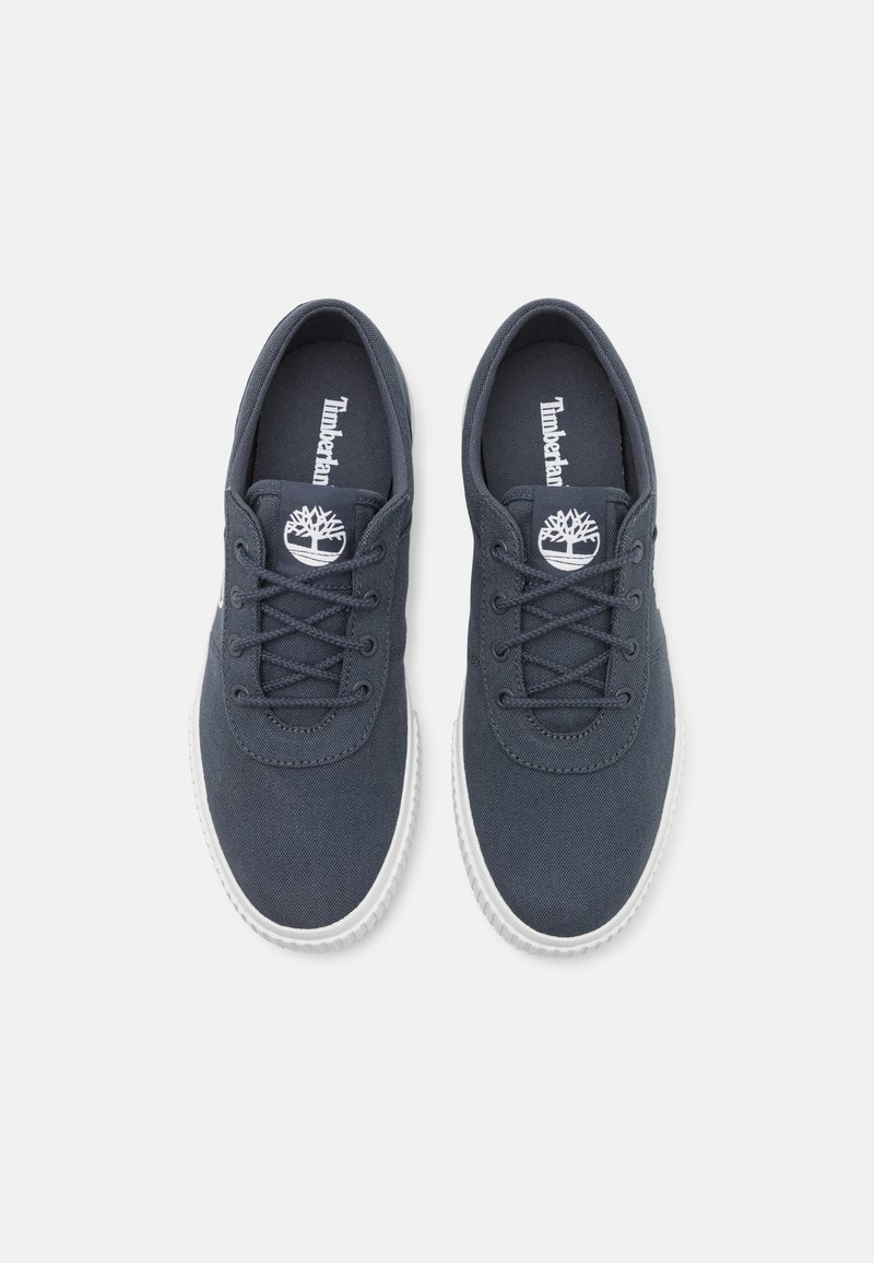 Zapatillas de lona azul oscuro con suelas de goma blanca, punta redonda y diseño de cordones. Presenta el logo de Timberland en la lengüeta.